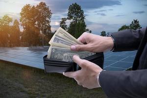 mano participación dólar cuentas ese Mira fuera de un billetera en un antecedentes de solar paneles ahorra dinero. utilizando solar energía. verde electricidad.