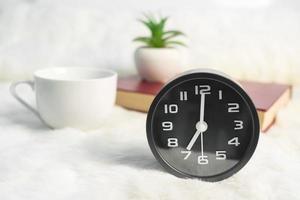 Black alarm clock and coffee cup  with book on table photo