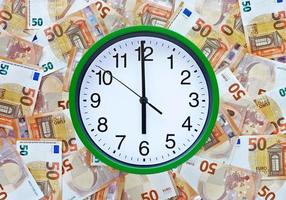 Big clock shows the time 6 am or pm, six o'clock in the morning or evening. The green clock centered on 50 fifty euro banknotes background. Euro currency in Europe. Time and money concept. photo