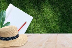 Notebook with pencil and straw hat on wooden table with green grass background,for art education background photo