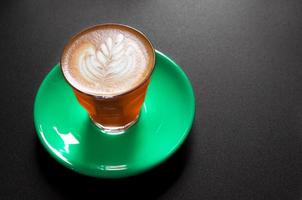 caliente latté en naranja y verde taza con floral modelo en espuma en un oscuro antecedentes foto