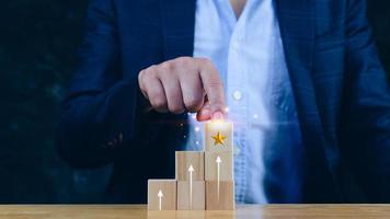 la mano del hombre de negocios elige el bloque de madera con el signo de la clasificación de estrellas formado garantía de calidad de servicio superior y flecha hacia arriba, garantía, concepto de estándares. foto