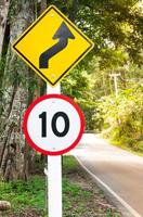señal de tráfico de límite de velocidad selectiva 10 y símbolo de precaución de carretera sinuosa para la conducción segura en carretera rural en bosque con vistas a la montaña, clave baja foto