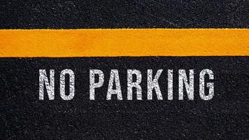 No Parking written and yellow line on the road in middle of the asphalt road, No Parking word on street. photo