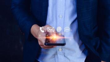 Customer support hotline Contact us people connection, Businessman using pointing touching Smart Phone with email, call phone, address, Chat message icons, Communication concept photo