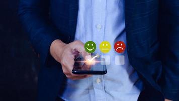 Businessman choosing happy smile face icon on SmartPhone. feedback rating and positive customer review experience, satisfaction survey. mental health assessment. photo