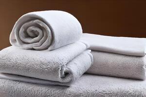 Clean white folded and roll towel nice and tidy stack each other at the table for fitness, bath, swimming, massage and spa marketing background and design material isolated on brown background. photo