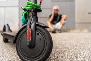 viajero diario al trabajo hipster hombre con eléctrico scooter es utilizando teléfono inteligente en el afueras foto