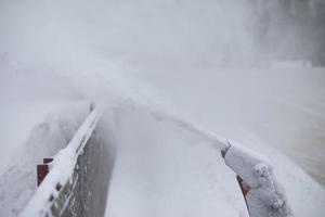 Snow ejection from ice rink. Snow removal equipment at hockey rink. Flow of fine particles from socket of machine. photo