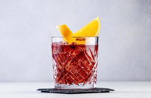 Negroni popular alcoholic cocktail with dry gin, red vermouth and red bitter, orange slice and ice cubes. Gray bar counter background, bar tools, copy space