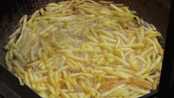 francês fritas estão frito dentro uma ampla Panela. fechar acima. rua Comida festival. batatas frito dentro óleo. 4k vídeo. video