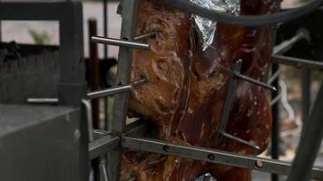 uma detalhado Visão do uma assado porco carcaça fiação em uma saliva. rua comida, fechar-se. video