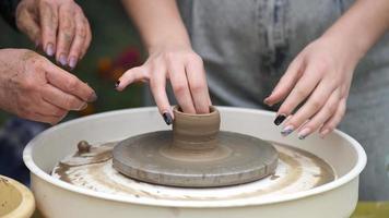 An elderly female craftsman teaches a young girl how to make pottery on a potter's wheel. Hands close-up. video