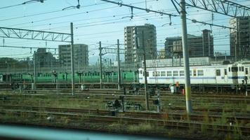 vista da janela do vagão de trem enquanto se move com a trilha ferroviária e muitos trens suburbanos e a cidade da área habitante local de fukuoka video