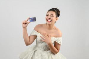 joven novia asiática hermosa publicando con tarjeta de crédito en la mano foto