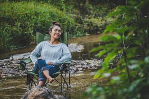 mujer joven sentada en una silla de camping en el arroyo para relajarse foto