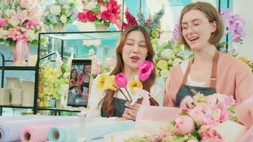 E-commerce business, two young female florist workers demonstrate and show floral arrangements via online live streaming with smartphone application in bright flower shop, a beautiful blossoms store. video