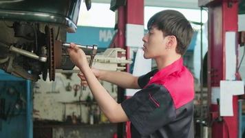 un Jeune expert asiatique Masculin automobile mécanicien technicien est baise voiture roue des noisettes sur levage avec clé pour réparation à garage. véhicule entretien un service travaux, industrie Occupation affaires emplois.