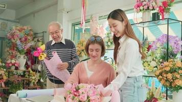 fiore negozio squadra, giovane bellissimo femmina fioraio lavoratori con vecchio proprietario organizzazione e decorazione mazzo di fresco fiori, sorridente con contento opera nel colorato negozio, piccolo attività commerciale pmi imprenditore. video