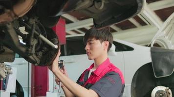 One young expert Asian male automotive mechanic technician is screwing car wheel nuts on lifting with wrench for repair at garage. Vehicle maintenance service works, industry occupation business jobs.