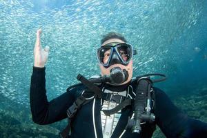 Scuba diver underwater selfie in the deep blue ocean and backlight sun and sardines bait ball photo