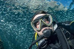 retrato de buzo mientras bucea dentro de una escuela de peces bajo el agua foto