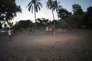 gili asahan, indonesia - 22 de agosto de 2016 - los niños juegan al fútbol al atardecer en un campo de palmeras cerca de la playa foto