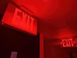 A red Exit sign. Emergency exit direction indicator on the ceiling in administrative building. Exit warning indicator for public safety in case of emergency photo