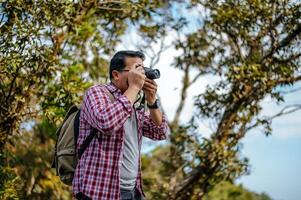 Young backpacker man use camera to take pictures in forest. photo