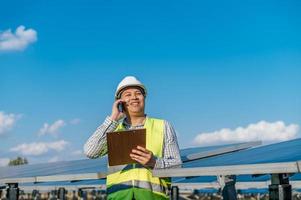 Young engineer talking on smartphone while working at solar farm photo