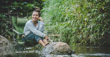 Young woman sitting on camping chair in stream for relax photo