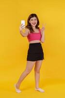 Portrait of Smiling young woman selfie with mobile phone in her hands while standing isolated over yellow background photo