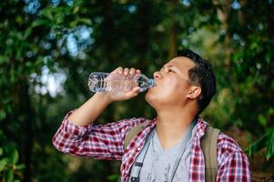 joven trekking bebida agua desde botella durante descanso en sendero foto