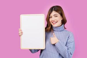 Portrait of Happy young woman holding an empty white placard over isolated pink background. photo