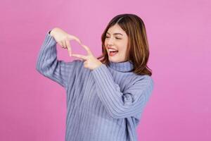 Portrait of Smiling young woman feels happy and romantic shapes heart gesture isolated over pink background photo