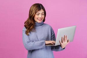Portrait of Happy young woman holding laptop in her hands while standing isolated over pink background. Technology and Business concept. photo
