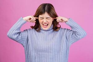 Portrait of Annoyed woman sticking plug fingers in ears not listening to loud noise sound isolated over pink background photo