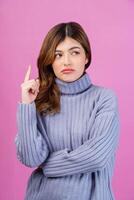 Portrait of young woman pointing finger up and thinking isolated over pink background photo