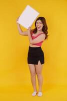 Portrait of Happy young woman holding an empty white placard over isolated yellow background. photo