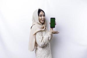 A portrait of a happy Asian Muslim woman wearing a hijab, showing her phone screen, isolated by white background photo