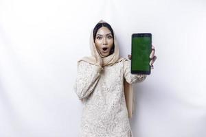 Shocked Asian woman wearing hijab, showing copy space on her phone screen, isolated by white background photo