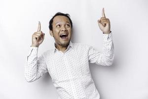 Excited Asian man wearing white shirt pointing at the copy space on top of him, isolated by white background photo