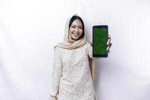 A portrait of a happy Asian Muslim woman wearing a hijab, showing her phone screen, isolated by white background photo
