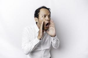 Young handsome man wearing a white shirt shouting and screaming loud with a hand on his mouth. communication concept. photo