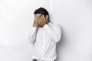 Young scared Asian man isolated on white background, looks depressed, face covered by fingers frightened and nervous. photo