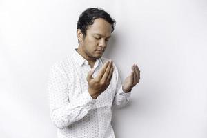 Religious Asian man wearing a white shirt praying to God, isolated by a white background photo