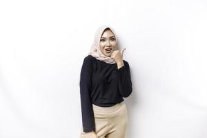 Excited Asian Muslim woman wearing a hijab gives thumbs up hand gesture of approval, isolated by white background photo