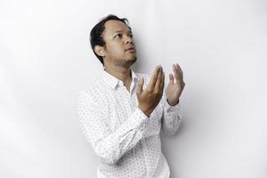 Religious Asian man wearing a white shirt praying to God, isolated by a white background photo