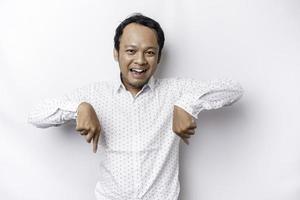 Excited Asian man wearing white shirt pointing at the copy space below him, isolated by white background photo