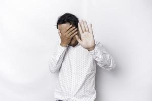 Young scared Asian man isolated on white background, looks depressed, face covered by fingers frightened and nervous. photo